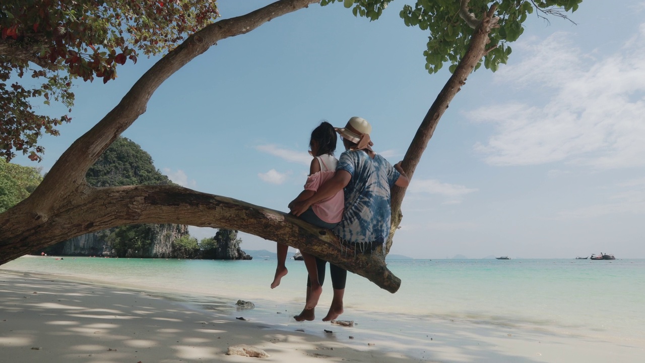 亚洲母亲和女孩坐在树上，享受大海视频购买