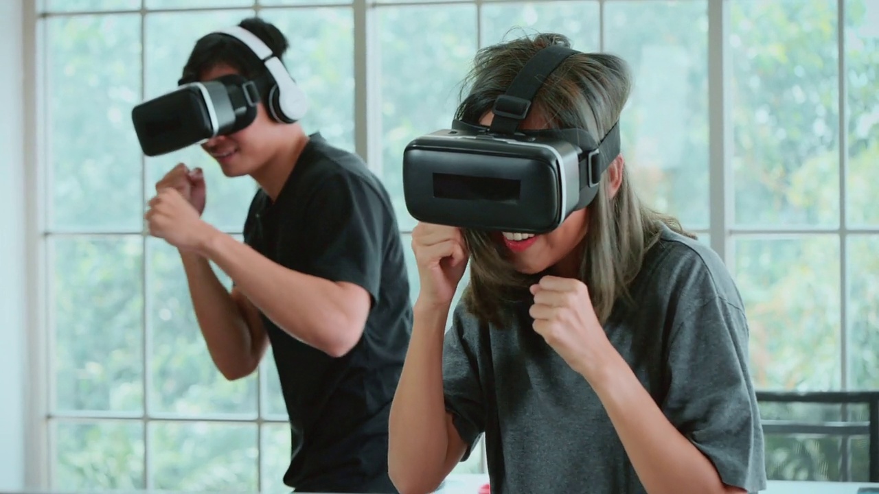 Metaverse，一对年轻夫妇在VR头戴式设备中玩拳击游戏，在家进行虚拟现实踢球训练。视频下载