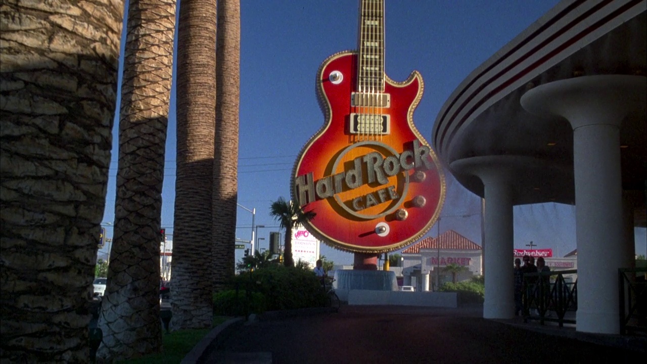 从棕榈树和蓝天上向下攀爬，来到硬石酒店或赌场外的“硬石咖啡馆”的吉他招牌上。餐馆。视频下载