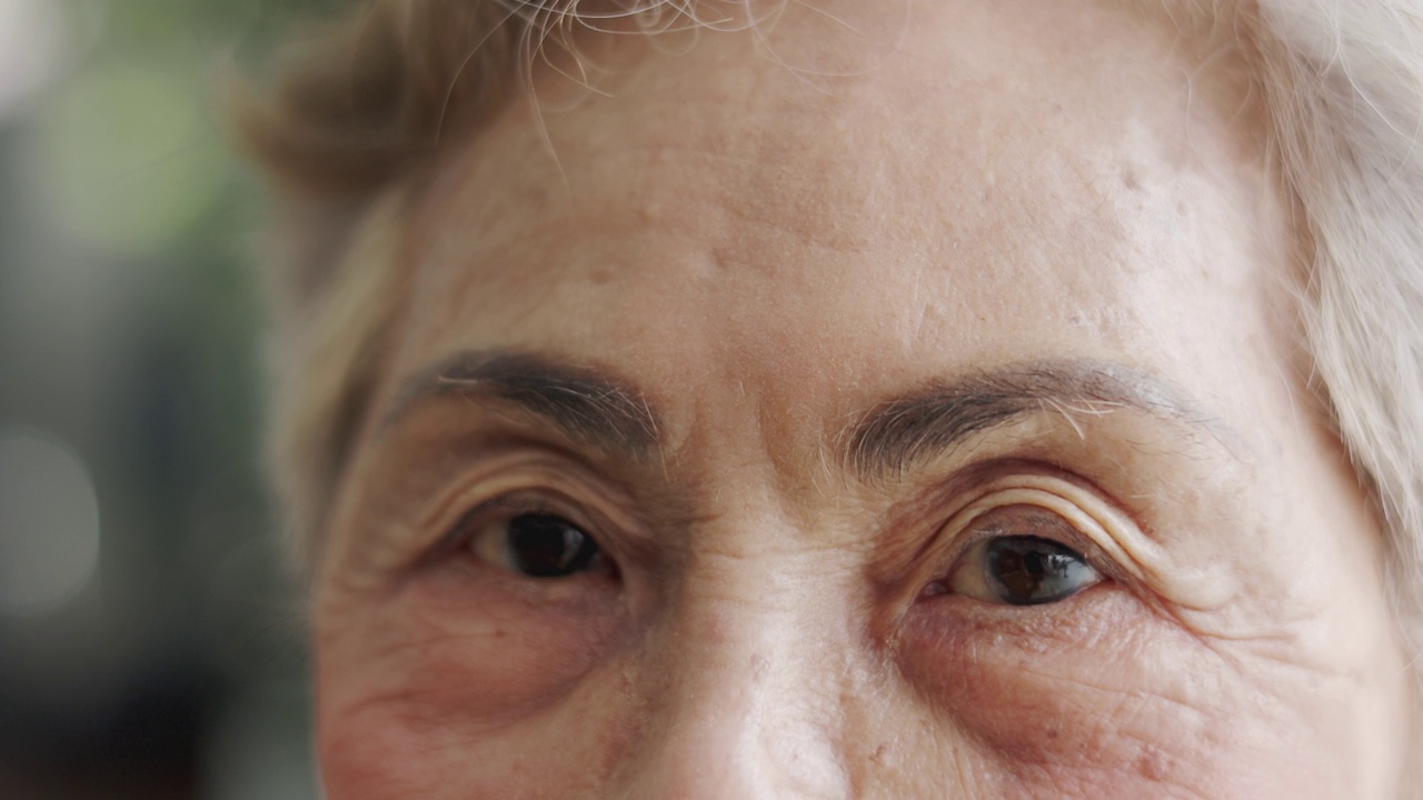 白发苍苍的亚洲老年女性(80岁)用眼睛直视镜头，近距离观察脸部和眼睛，脸上布满皱纹，洋溢着享受退休生活的快乐。视频素材