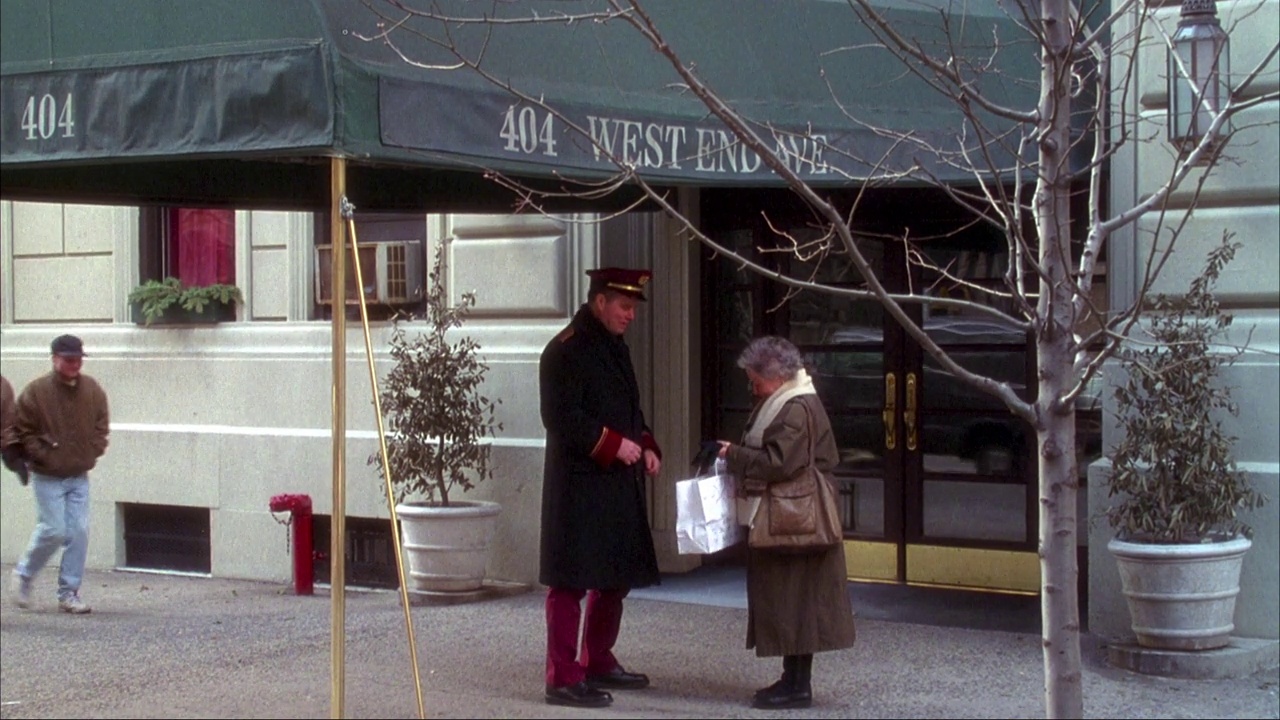 中景公寓入口，看门人与老妇人交谈。入口有绿色的天篷，上面写着“404 west end ave”。两者都进入大楼，平移到三楼的一扇窗户上。视频下载