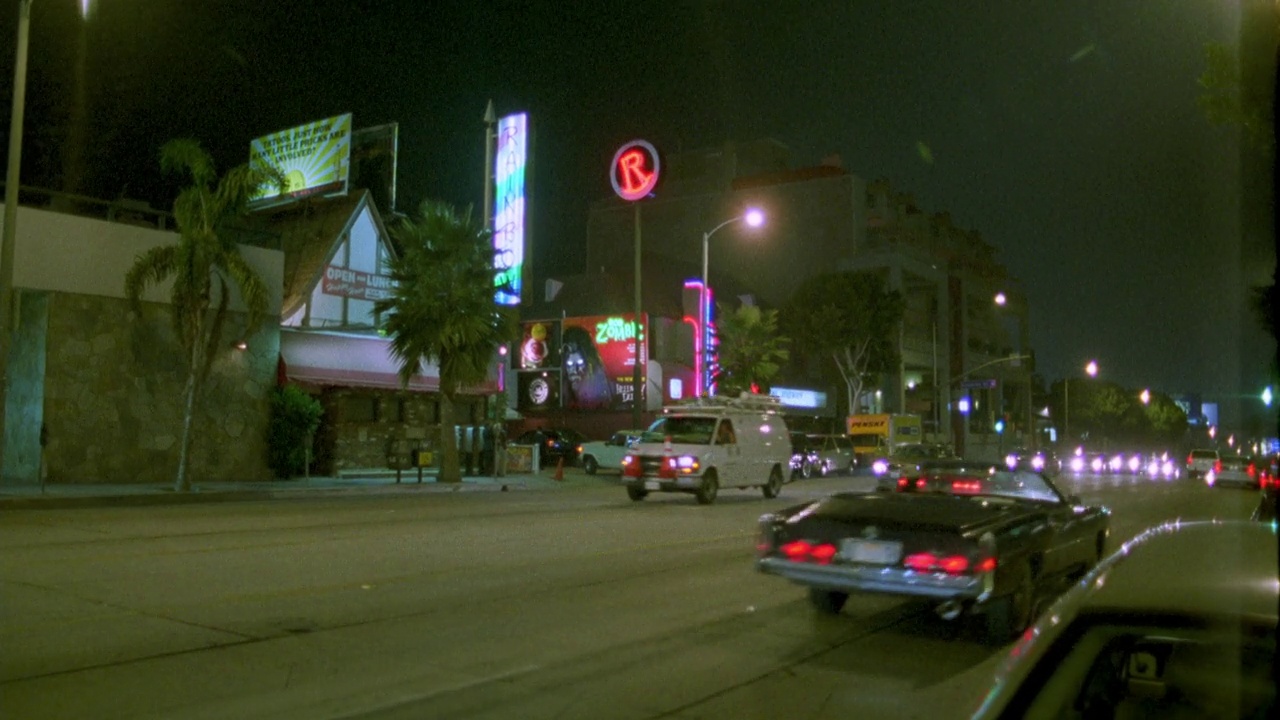 从左到右行驶在日落大道上的汽车。棕榈树和路灯排列在街道两旁。霓虹灯和酒吧。洛克西酒吧和音乐俱乐部。西好莱坞。日落大道。视频素材