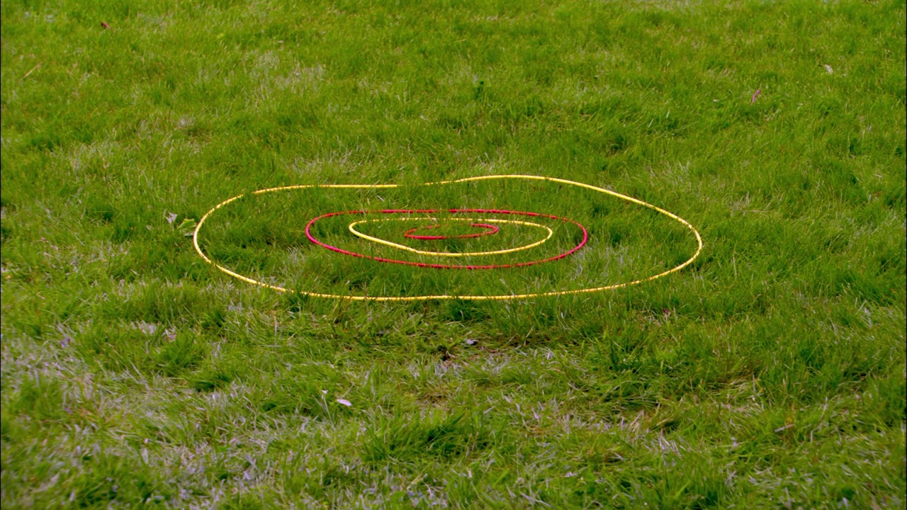 在草地上的一个环的目标的中等角度。可能是草坪飞镖。戒指在红色和黄色之间变化。黄色和蓝色的飞镖被扔向目标，但都没有射中。视频下载