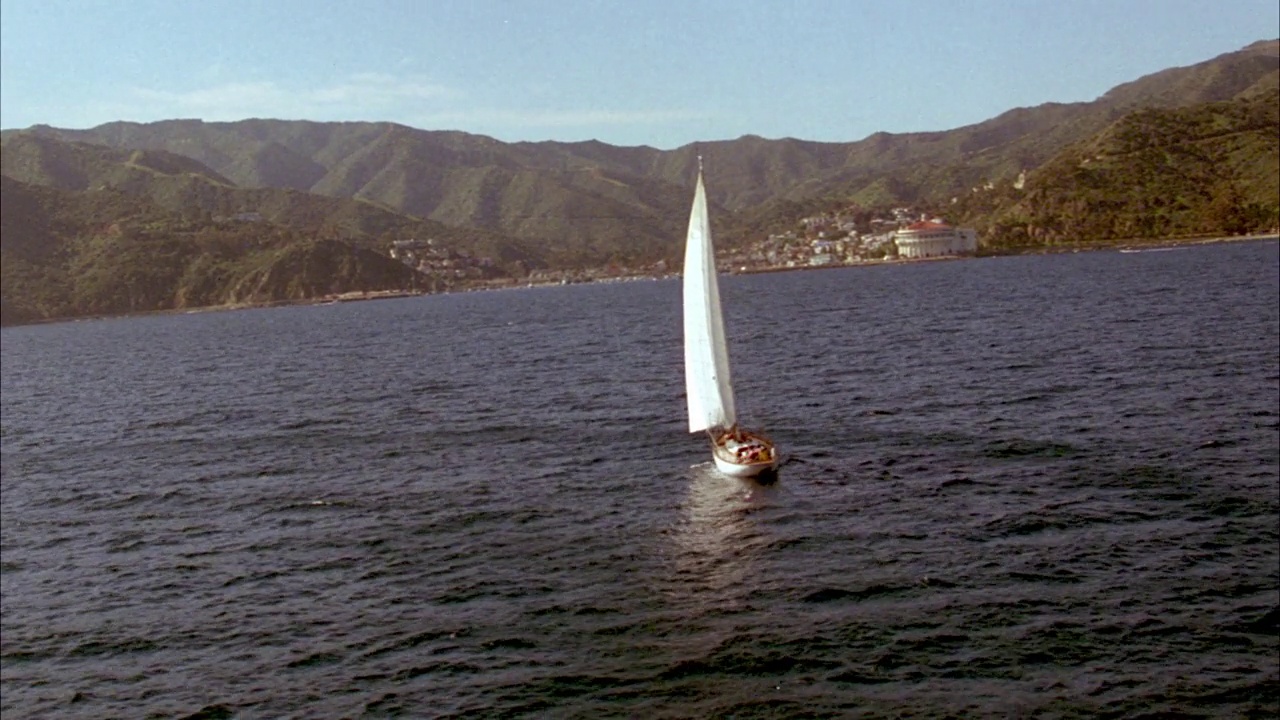 帆船和海洋的航拍，背景为卡特琳娜岛和阿瓦隆岛。绕到后面挂着美国国旗的白色单桅帆船的右边。视频素材