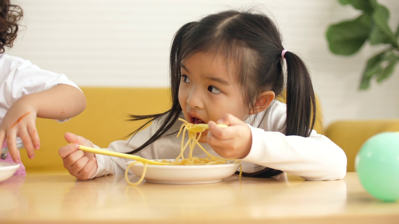 小女孩在家里吃着凌乱的意大利面，快乐可爱的孩子在吃意大利面时把盘子弄得一团糟。有趣的蹒跚学步的孩子用家里做的意大利面和番茄酱视频下载