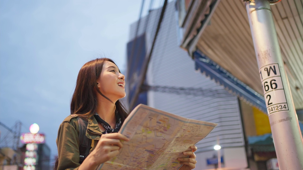 亚洲年轻女背包客在地图上寻找目的地。迷人美丽的旅游女孩独自在街上旅行，享受步行在城市的夜晚在泰国度假旅行视频购买