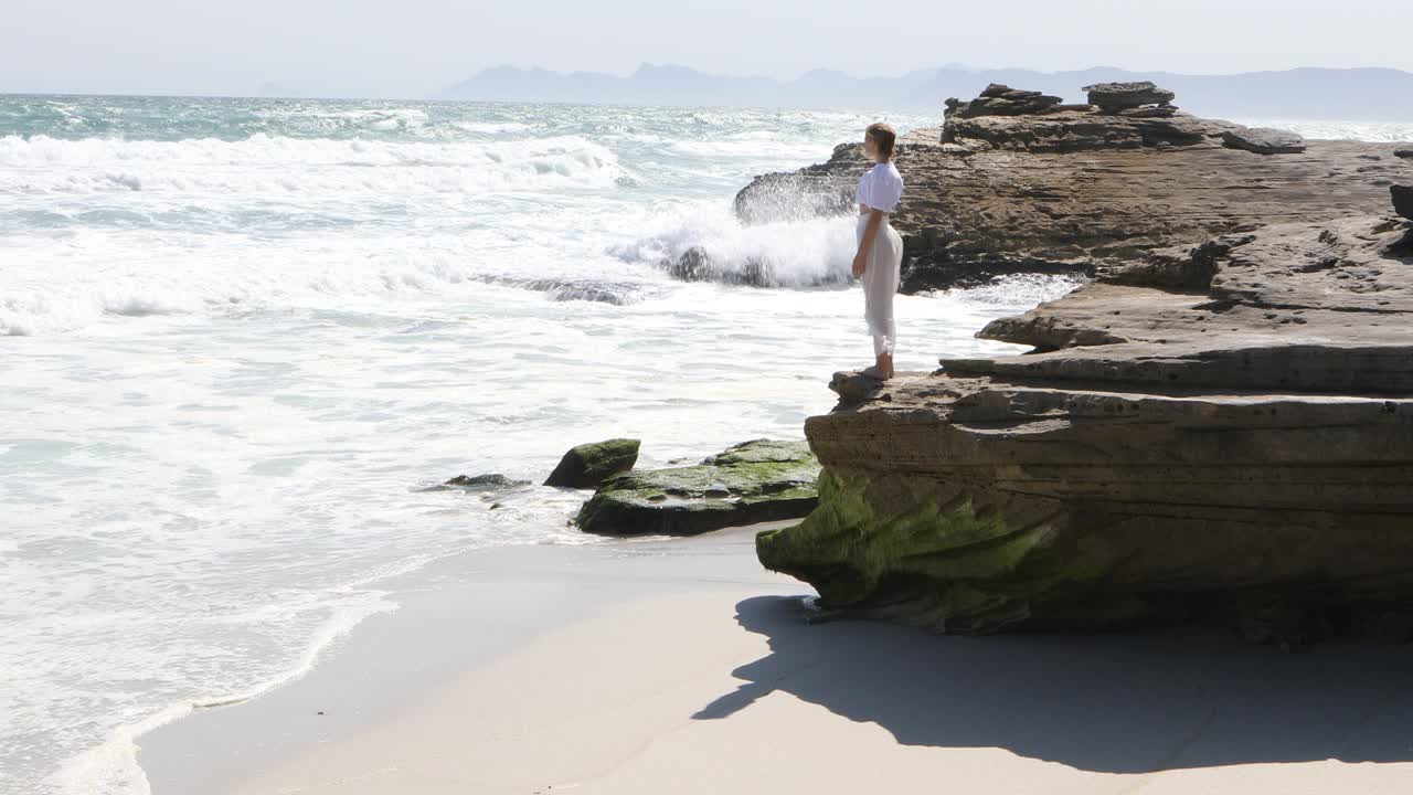 一个十几岁的女孩在海边探索岩石视频素材