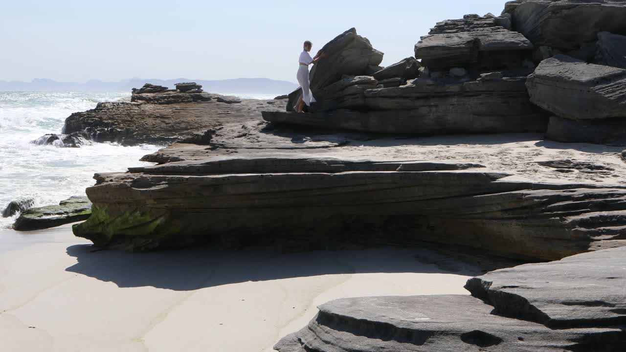 一个十几岁的女孩在海边探索岩石视频素材