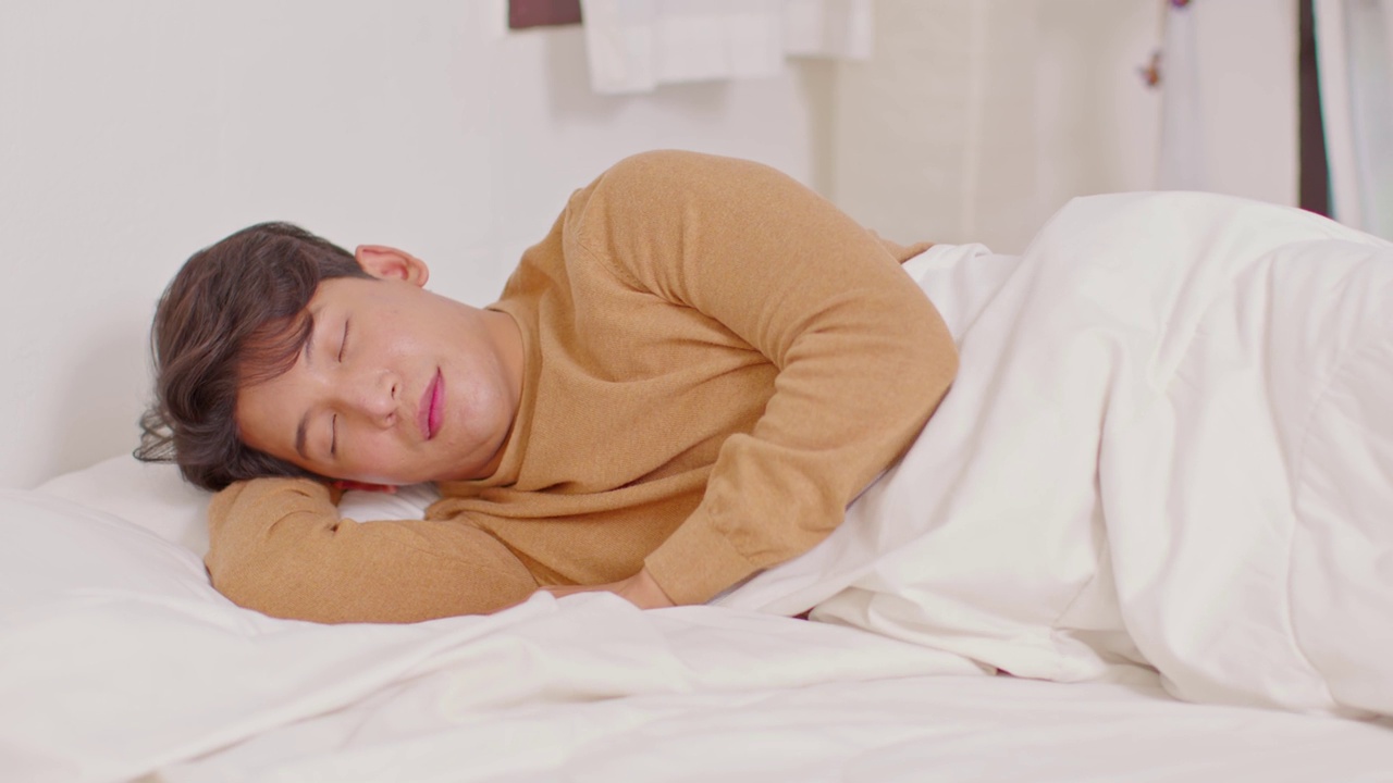 英俊迷人的亚洲男人睡觉和甜蜜的梦躺在床上舒适的卧室早上感觉如此放松和舒适。健康的年轻男性在家就寝。医疗保健的概念视频购买