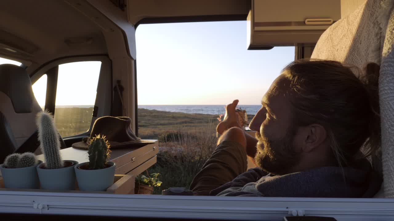 慢镜头:一名男子乘坐露营车在日落时分欣赏美丽的海景视频下载