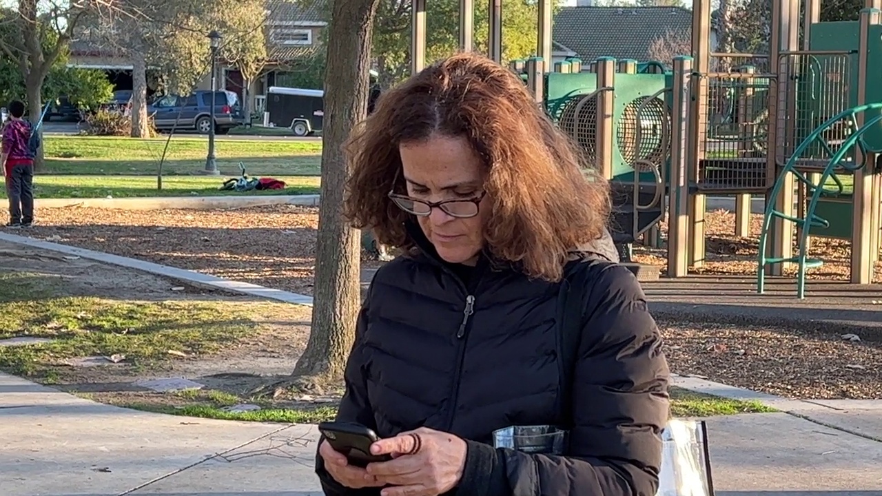 成熟的女人在公园里用她的智能手机视频素材