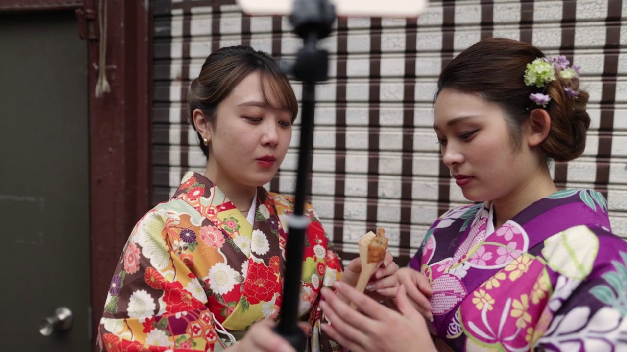 穿着和服的年轻女性朋友为了拍视频而吃街头小吃视频素材