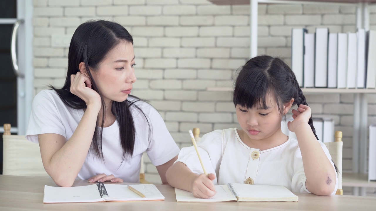 愤怒的年轻亚洲母亲生气的小女儿教和做作业写。她坐在家里的书桌前听不懂。孩子的教育问题，父母和孩子的冲突。视频素材