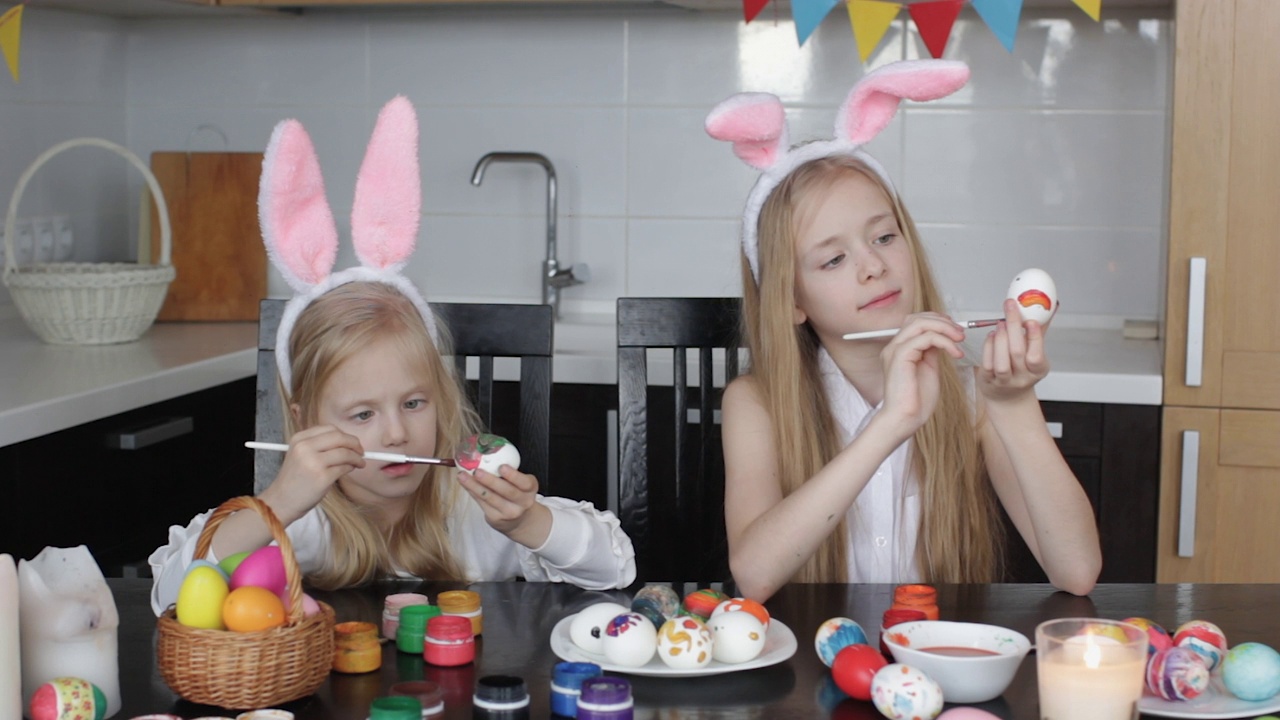 两个长着兔耳朵的小女孩正在画复活节彩蛋，孩子们正在为春节做准备，视频下载