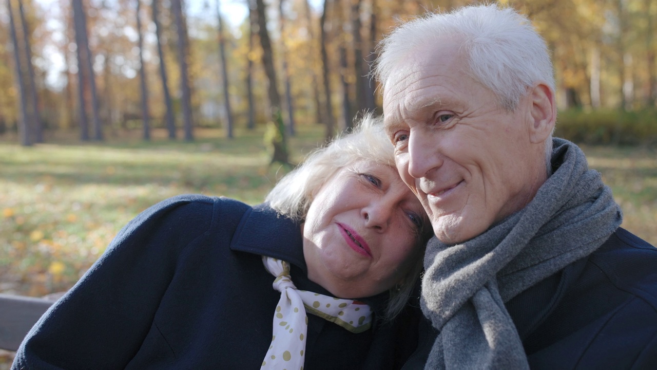 成熟的情侣抱在一起，坐在阳光明媚的秋日公园的长椅上，幸福的一家人视频素材