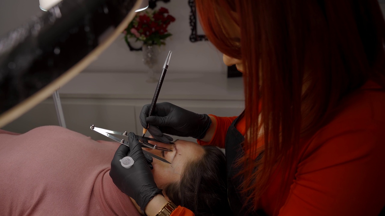 主美容师的手的侧面视图测量眉毛的比例，用特殊的工具涂上颜料。microblading的概念视频下载