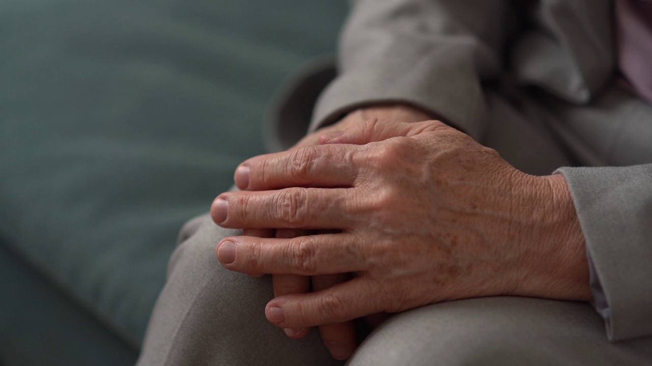 一个无法辨认的老年妇女的手部特写。成熟的女人双手合十，膝盖上满是皱纹和老年斑。年老的时候视频下载