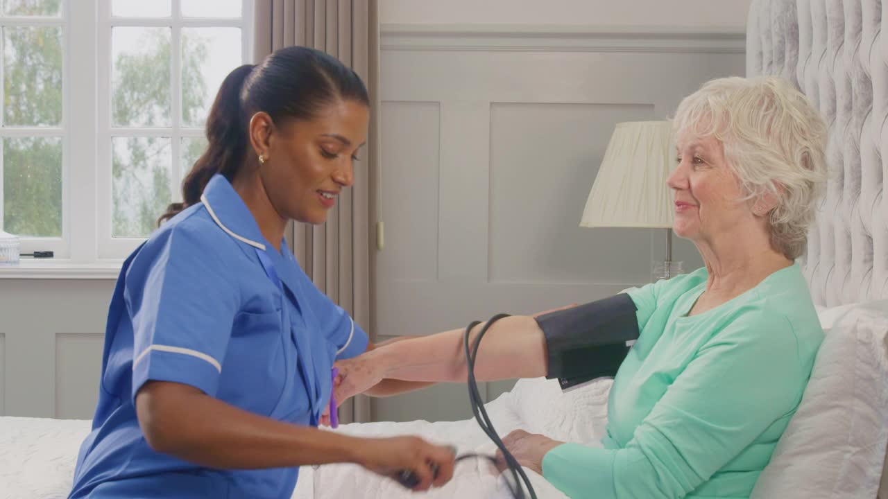 在家中卧床的老年妇女，由穿着制服的女护理人员测量血压视频素材