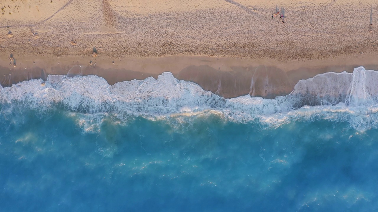 希腊莱夫卡达的米洛斯海滩。从上往下看，金色的沙滩和荧光的绿松石色的海浪。在日落时分欣赏夏日美景的人们视频下载