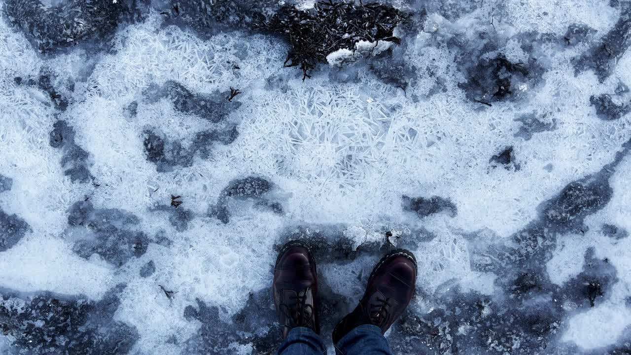 穿靴子的人踩在冰上，使冰在结冰的湖面上裂开视频素材