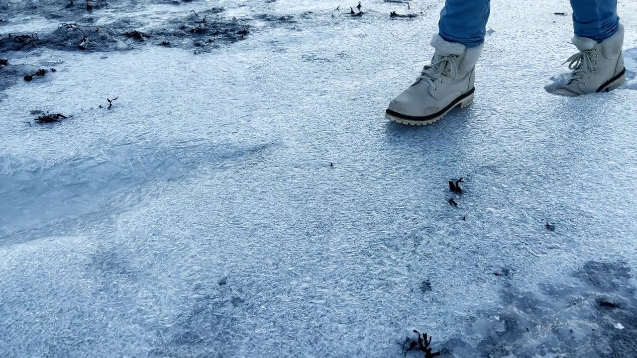 一个穿着靴子的女人走在结冰的海滩上，却被冰绊倒了视频素材
