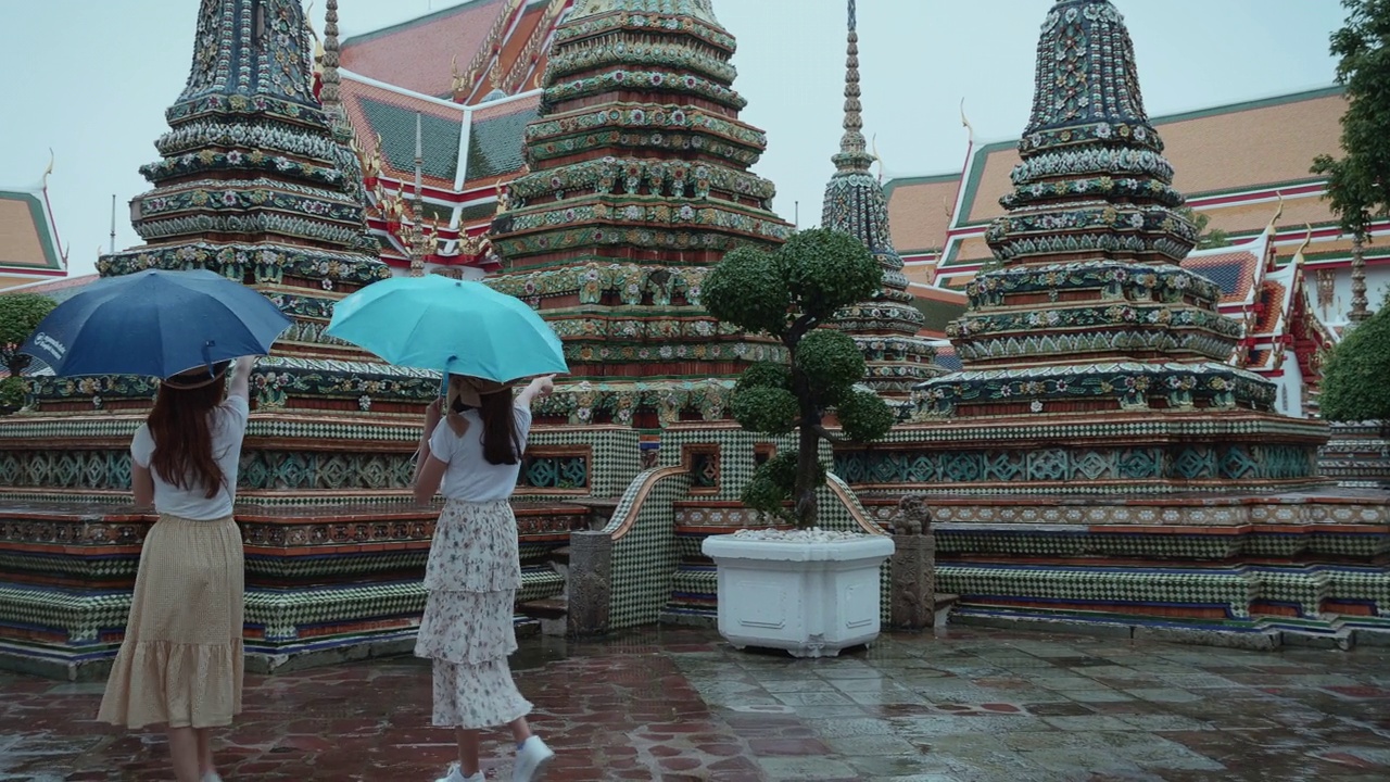 美丽的年轻游客在雨中撑开雨伞，走着，享受和幸福地看卧佛寺在泰国曼谷。后视镜是意外拍摄的地标/著名的地方。缓慢的,视频素材