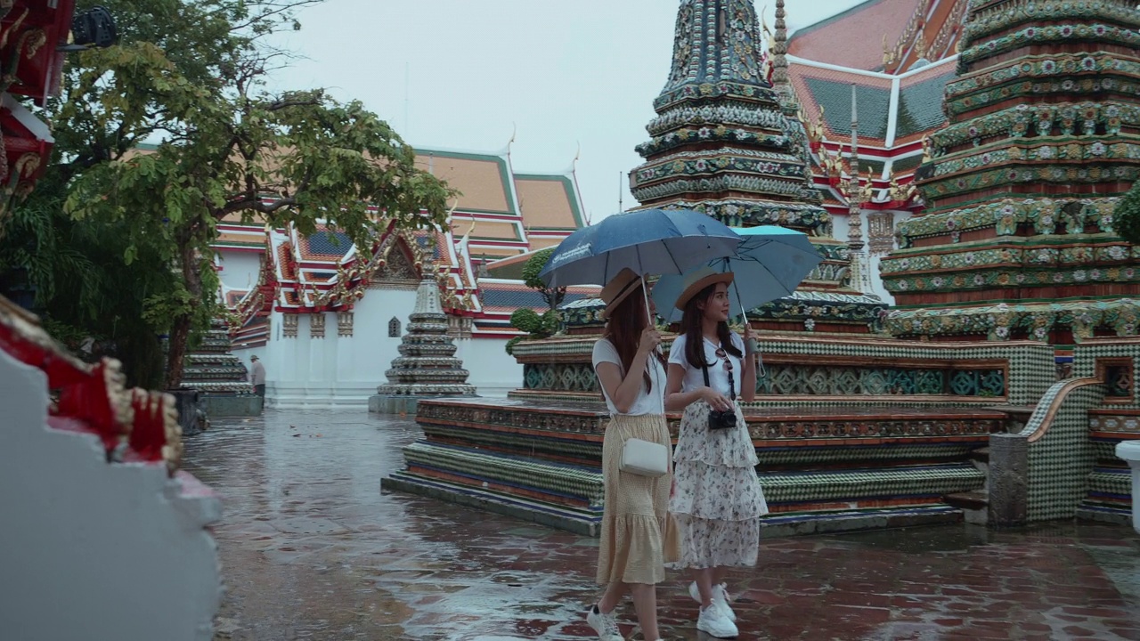 美丽的年轻游客在雨中撑开雨伞，走着，享受和幸福地看卧佛寺在泰国曼谷。后视镜是意外拍摄的地标/著名的地方。缓慢的,视频素材