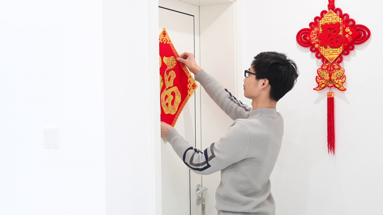 一位年轻的亚洲男子正在门上贴“福”字的春联视频素材