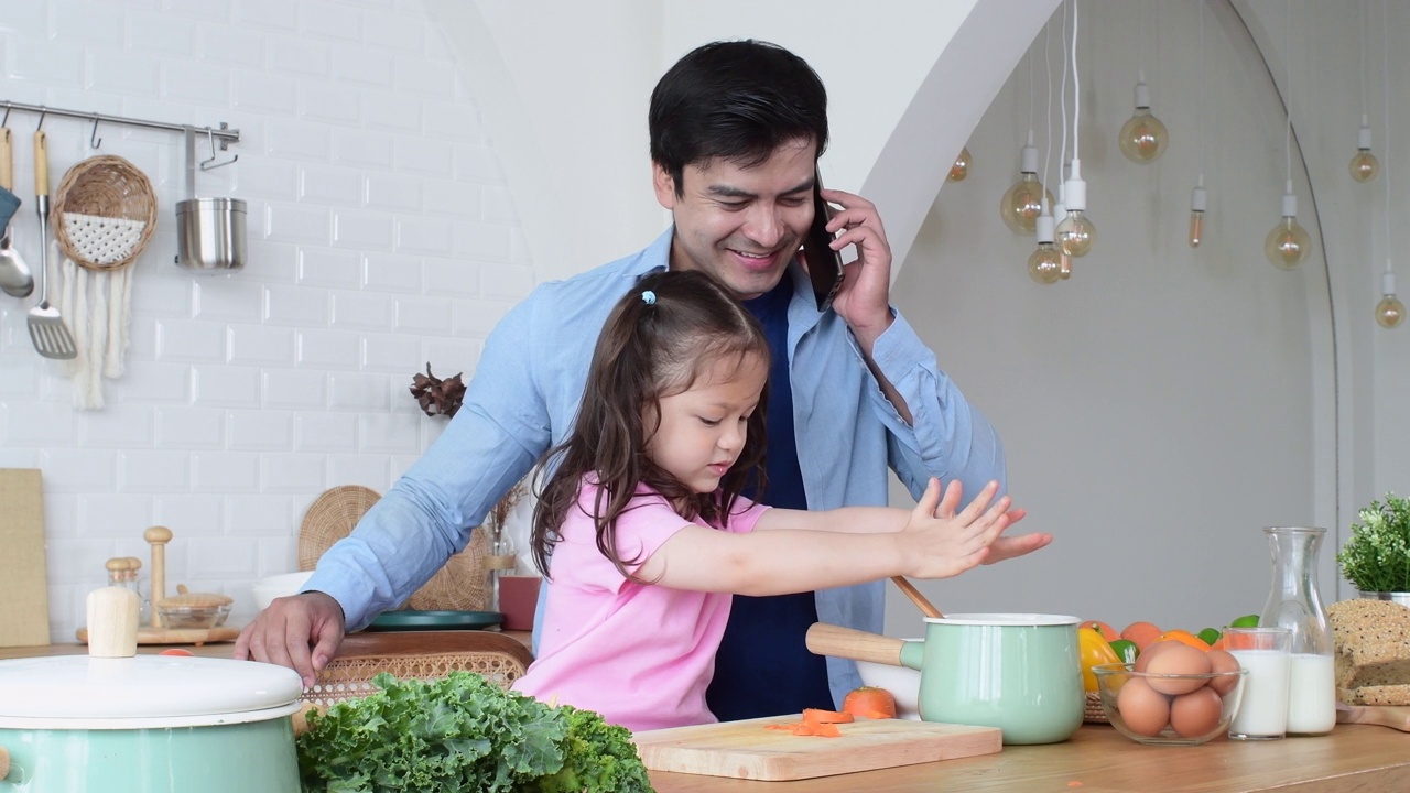 忙碌的父亲照顾女儿，而使用电话在柜台厨房交谈视频下载