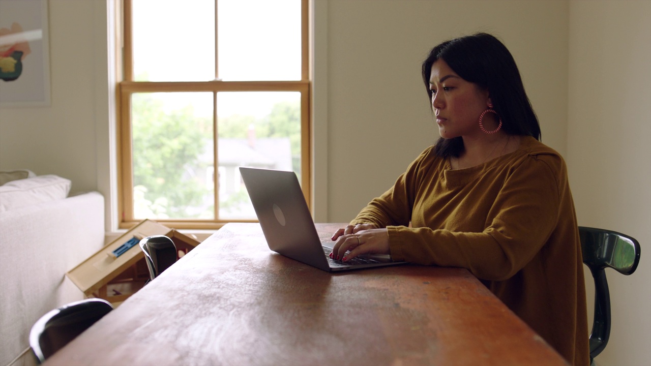 ZI Medium拍摄的是一个女人在家里客厅的桌子上用笔记本电脑工作视频下载