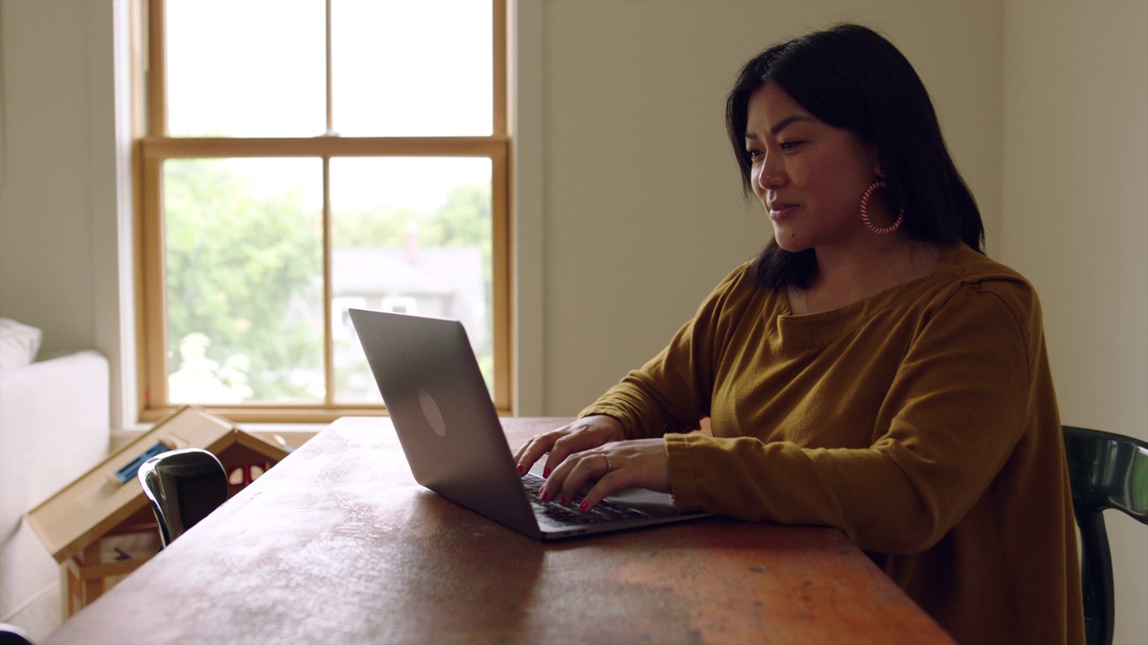ZI Medium拍摄的是一个女人在家里客厅的桌子上用笔记本电脑工作视频下载