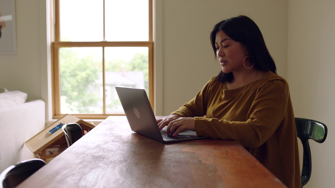 ZI Medium拍摄的是一个微笑的女人在家里客厅的桌子上用笔记本电脑工作视频下载