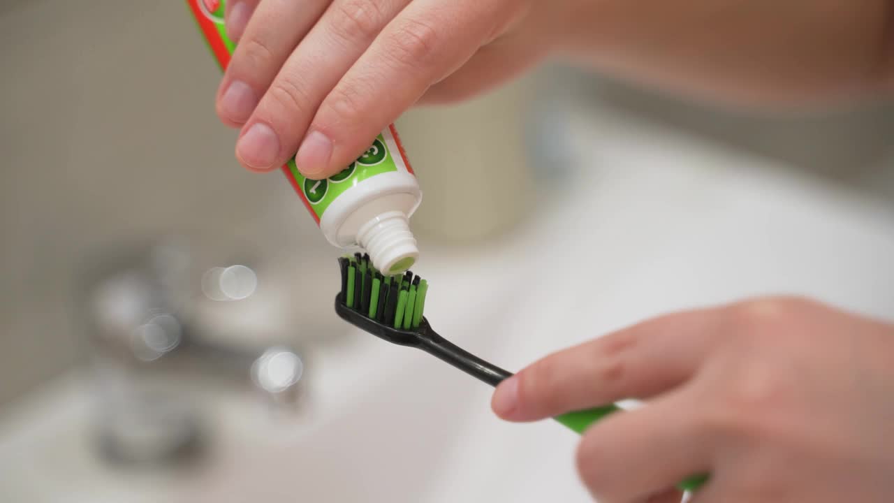 用黑色和绿色的牙刷从盥洗室的水槽上的牙膏管中挤出绿色牙膏。准备刷牙。牙齿护理，习惯，日常事务视频下载