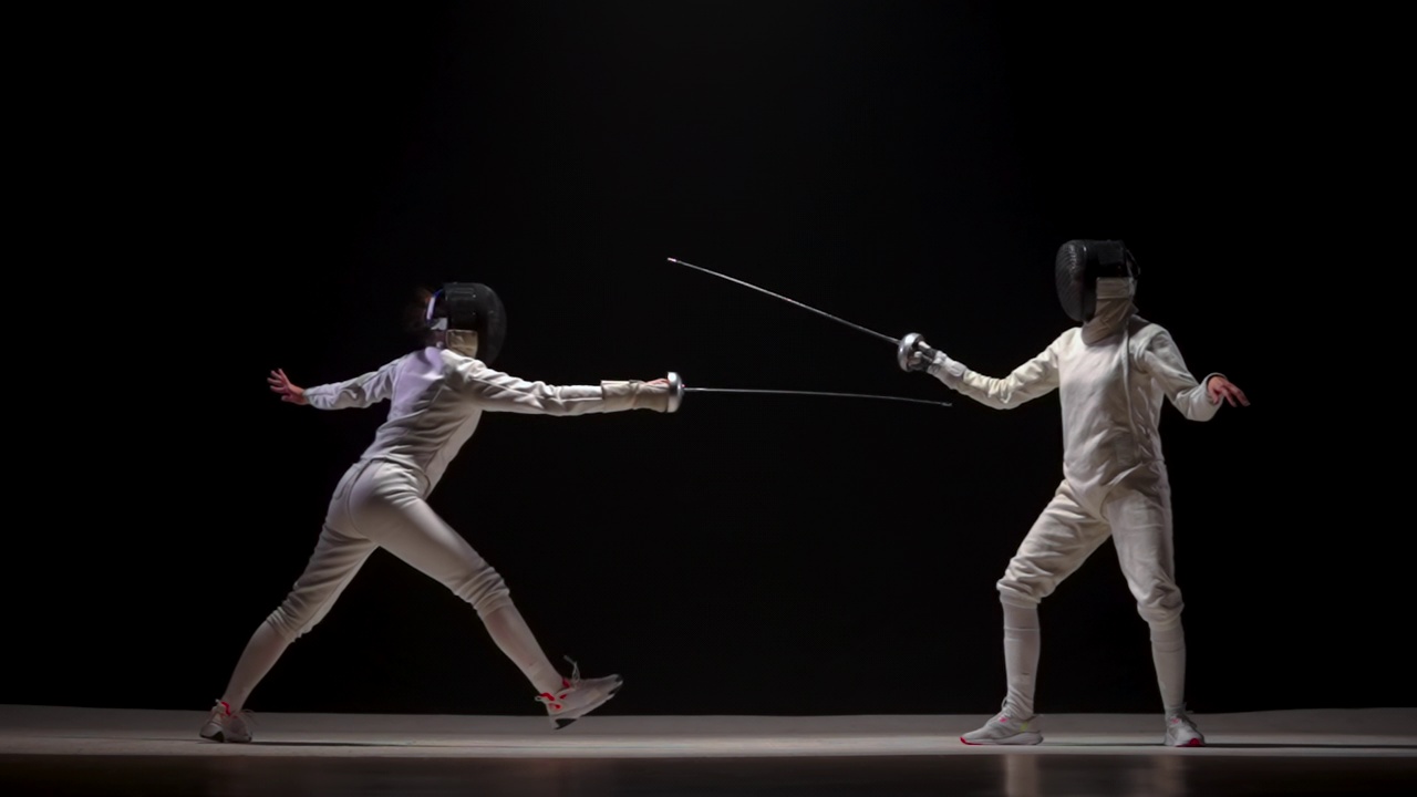 两名女子击剑手在黑色背景下对决。搭档示范剑术，练习攻击要素。身穿白色制服、戴着面具的运动员互相攻击。慢动作视频下载