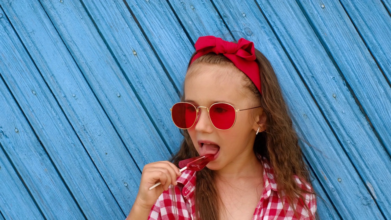 戴着红色太阳镜的女孩手里拿着一根三角形的棒棒糖，用舌头舔它。视频下载
