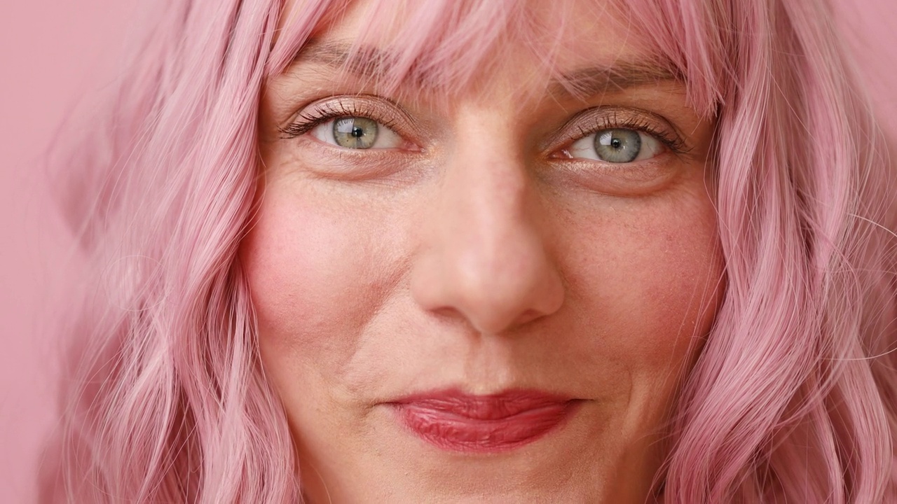 粉色头发的人类女性脸的特写镜头。女人与自然的脸美妆孤立在粉红色的背景视频下载