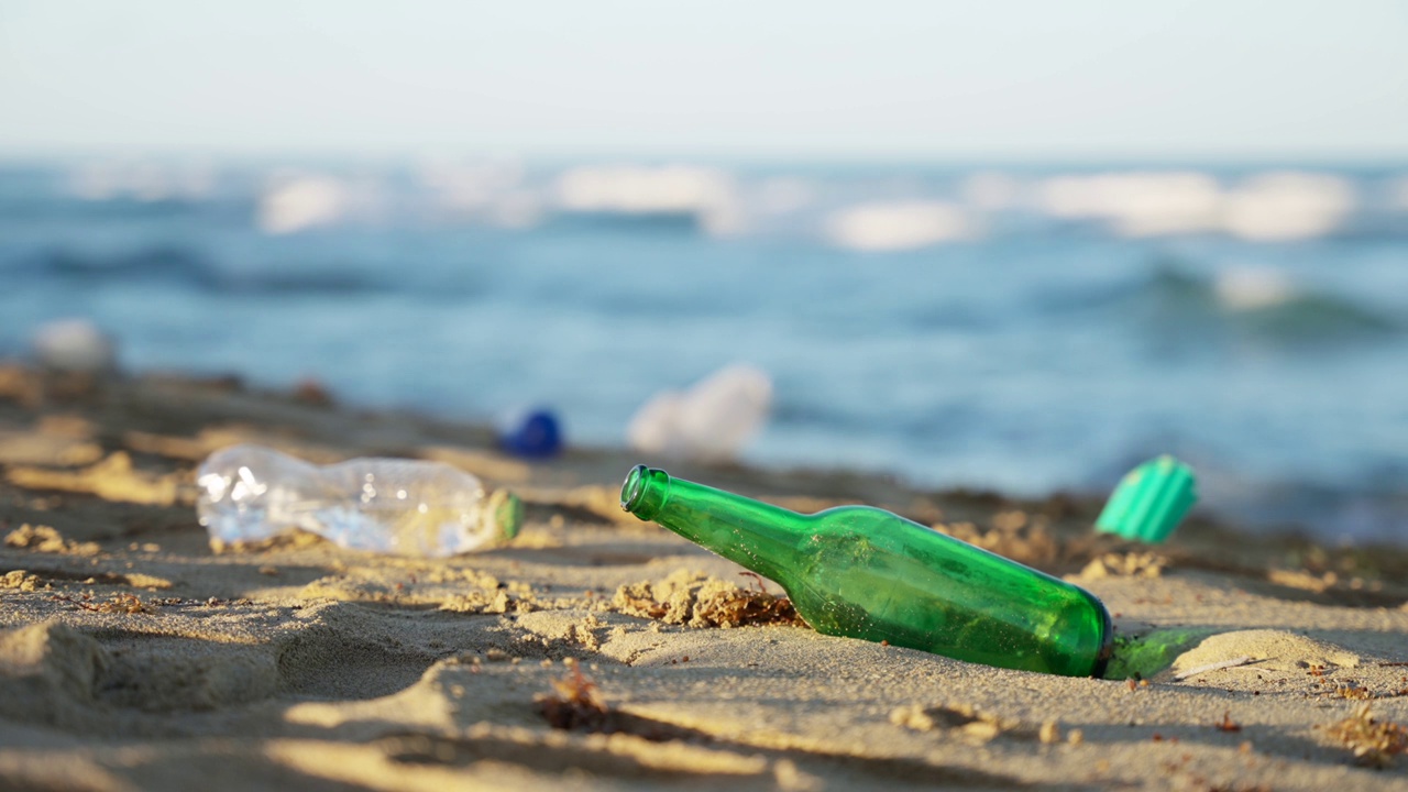 空的玻璃瓶子和塑料瓶子被扔在沙滩上。视频素材