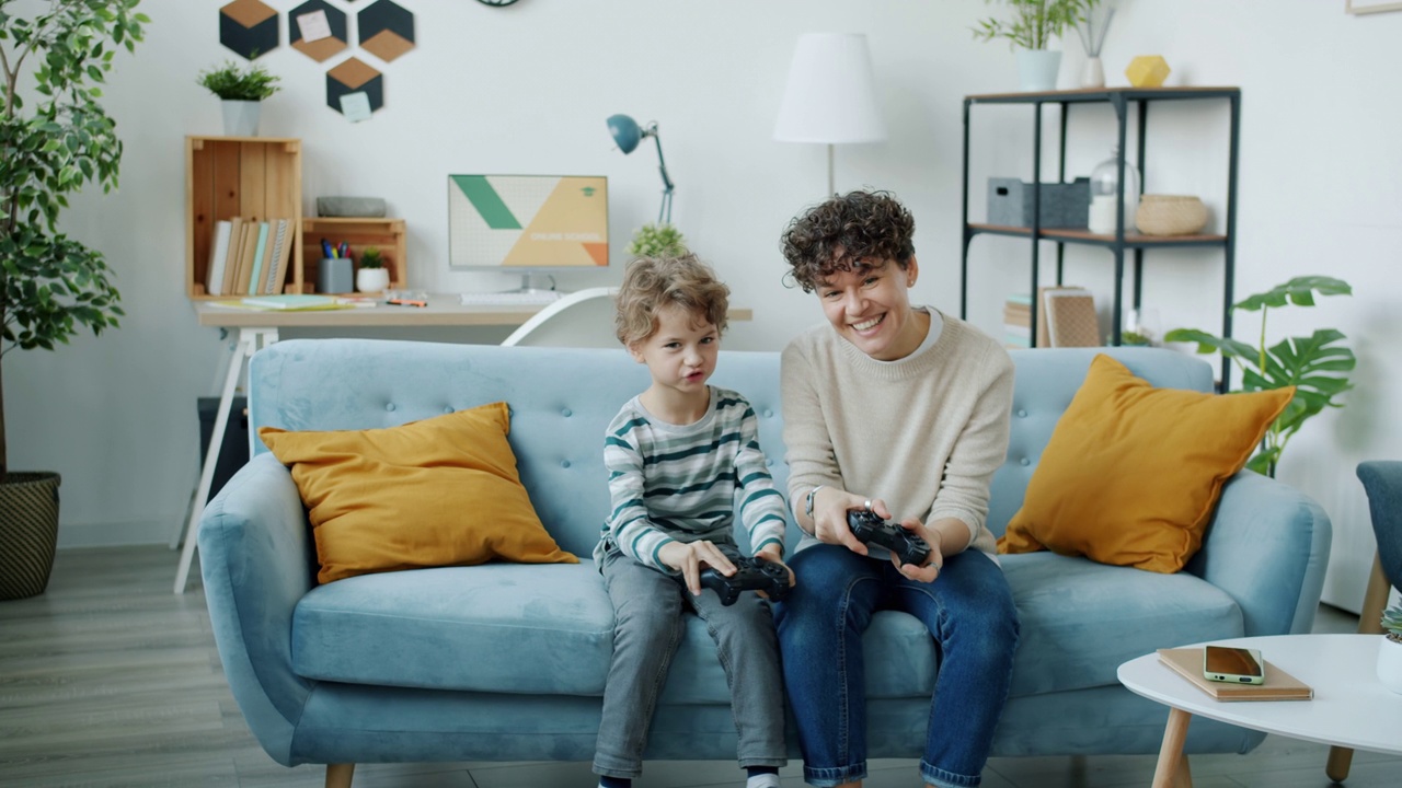 一个年轻的女人和儿子在公寓里一起玩电子游戏的慢镜头视频素材