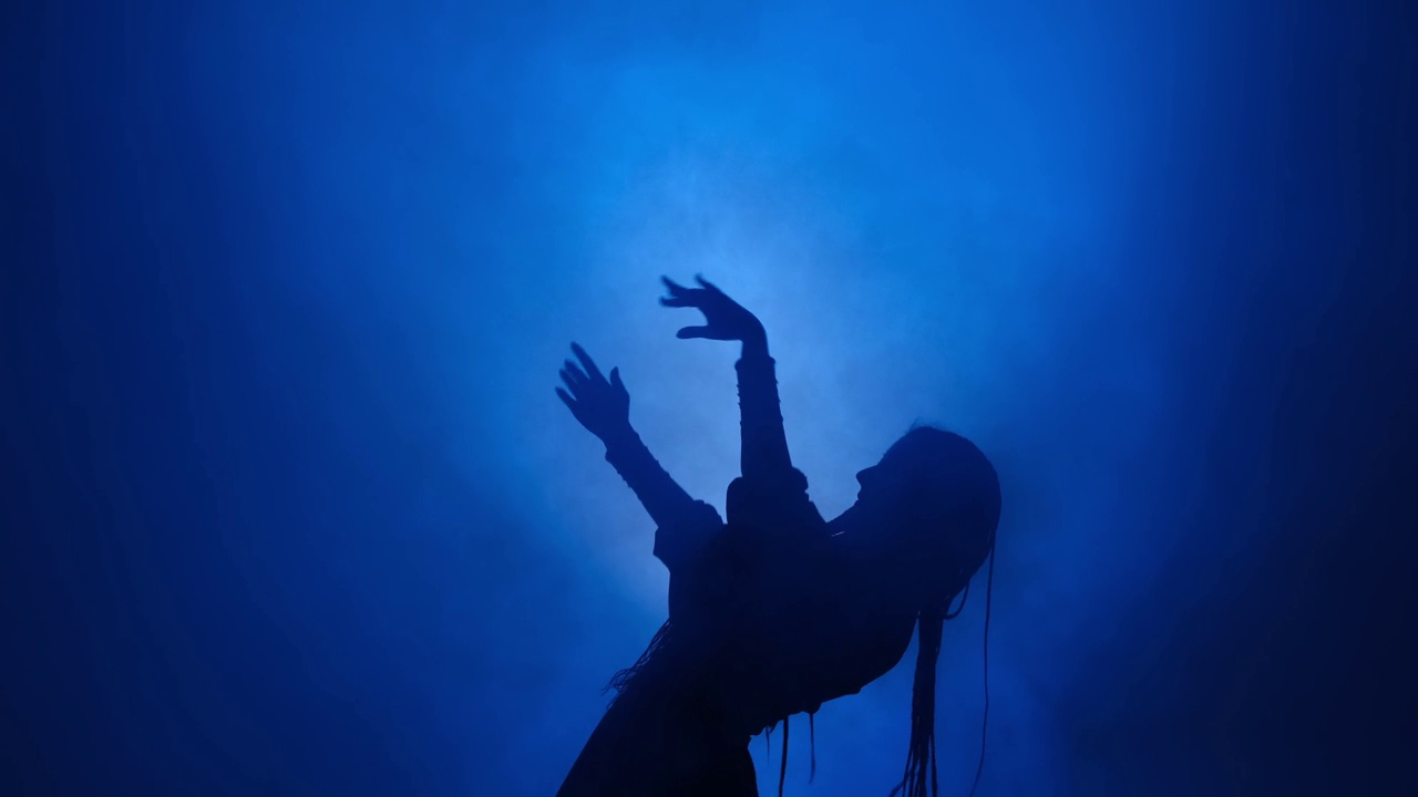 一个女人的剪影在蓝色的灯光和烟雾中跳舞视频下载