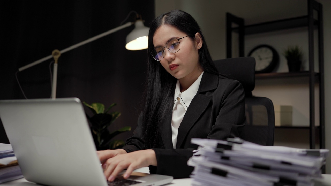 年轻的亚洲女商人工作到深夜。她忙着检查文件，不得不在截止日期前把工作发过去，感到压力很大。晚上坐在黑暗的办公室里。视频下载