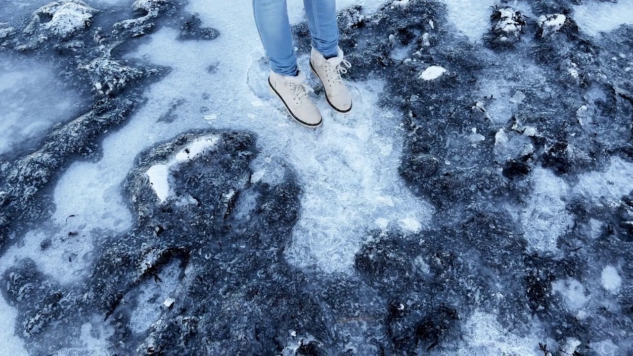 女人走在结冰的沙滩上踩在冰上，把它弄裂了视频素材