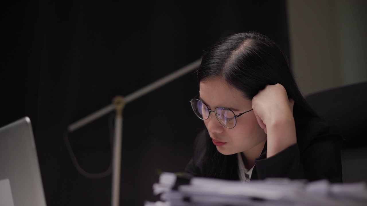 亚洲女商人晚上在黑暗的办公室里用手提电脑工作。聪明的女人工作努力，加班认真思考。深夜在温暖的灯光下感到压力和头痛视频下载