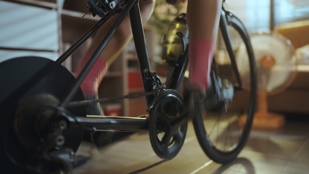 亚洲女人骑自行车。她正在房子里锻炼。通过骑自行车上的教练和玩在线自行车游戏视频下载