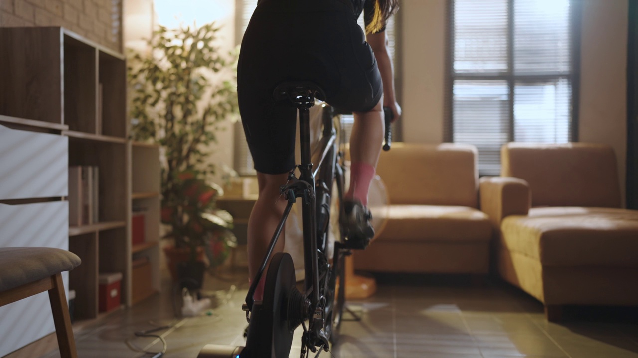 亚洲女人骑自行车。她正在房子里锻炼。通过骑自行车上的教练和玩在线自行车游戏视频素材