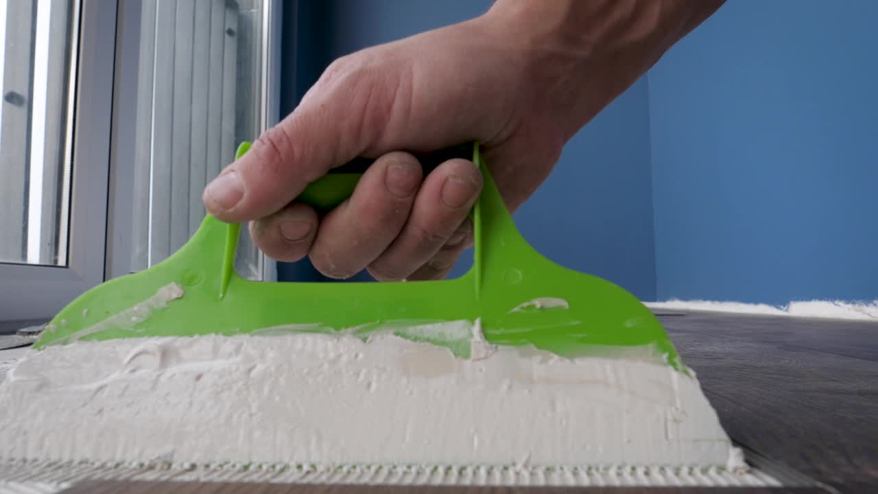 工人在涂胶乙烯基或层压板之前用刮刀在地板上涂上胶水视频素材
