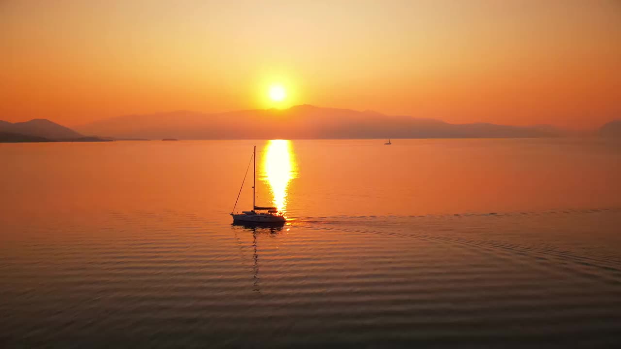 希腊爱奥尼亚海岸的日落。明亮的阳光，远处的陆地，漂浮的小船，水中的倒影视频下载