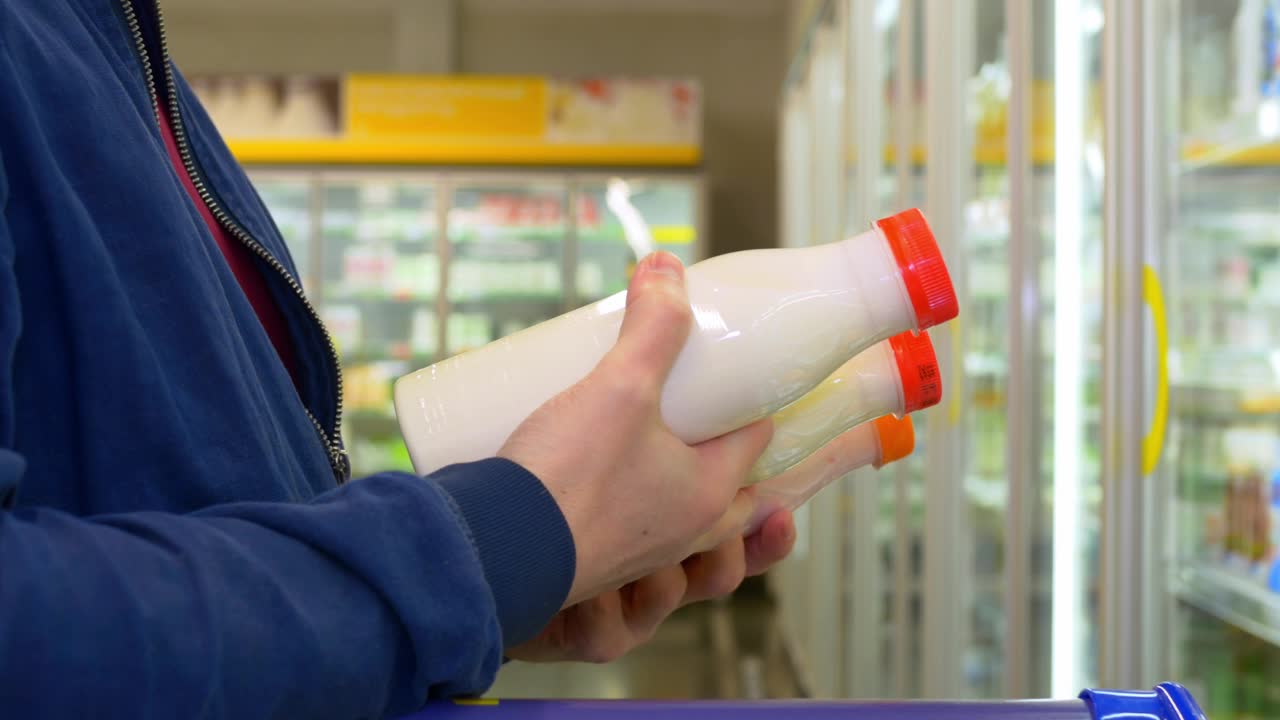 店里的买家挑选产品，仔细阅读成分，摇一瓶酸奶。一个男人在商店里挑选乳制品，手里拿着奶瓶视频素材