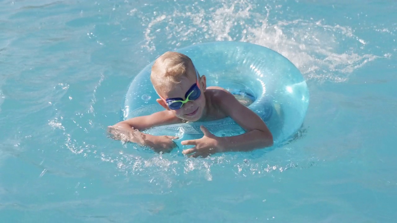 小男孩在游泳池里，孩子玩得很开心，坐在蓝色的游泳圈上，在水下玩耍。夏季旅游酒店度假游客视频下载