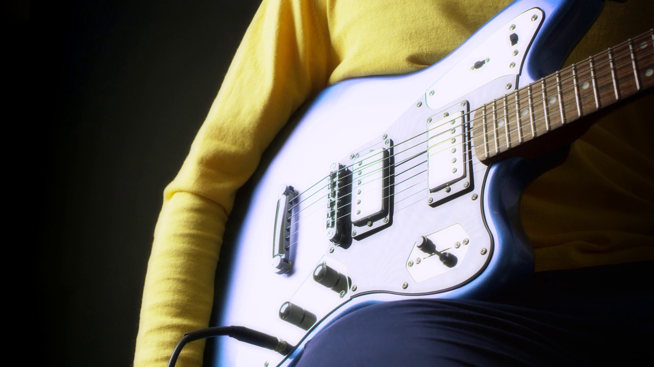 身穿黄色套头衫的男吉他手在黑色背景下弹奏电吉他视频下载
