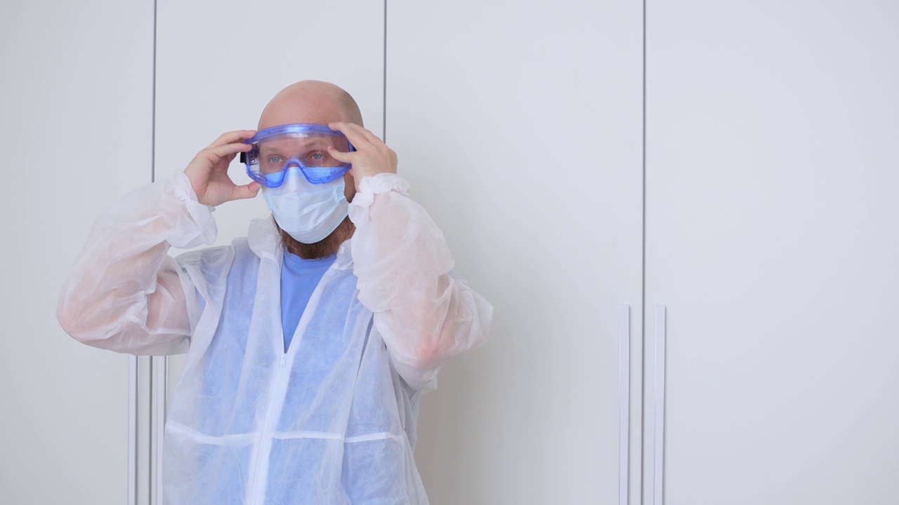 在新型冠状病毒大流行期间，更衣室里的医生穿上防护服，戴上口罩和护目镜，与感染者一起工作视频素材